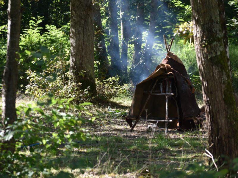 Tente de peaux et fumée d’un foyer en sous-bois, à l’Archéovillage