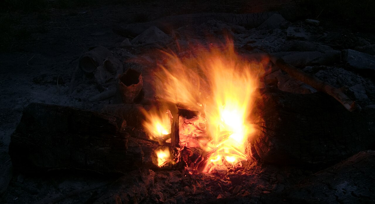Flammes d’un feu entretenu entre des pierres, la nuit