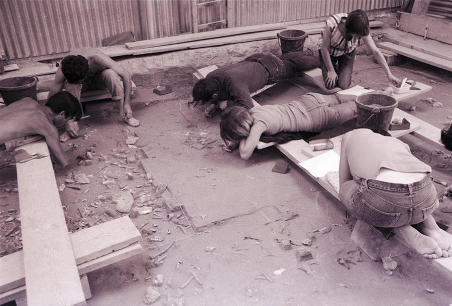 Des fouilleurs allongés sur des planches dégagent un sol d’habitation à Pincevent en 1967