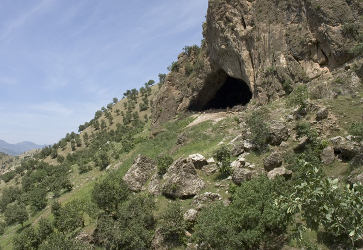 Vue extérieure de la grotte de Shanidar, deux personnes accroupies devant l’entrée pour l’échelle