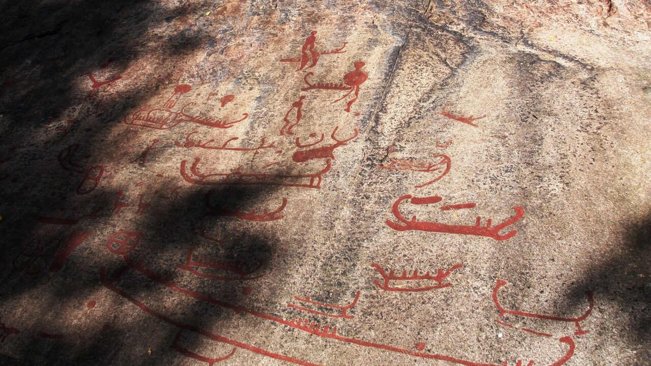Dalle de granit gravée de bateaux et de figures, peintes en rouge, dans l’herbe