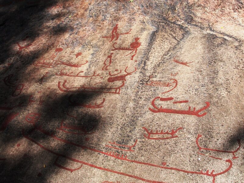 Dalle de granit gravée de bateaux et de figures, peintes en rouge, dans l’herbe
